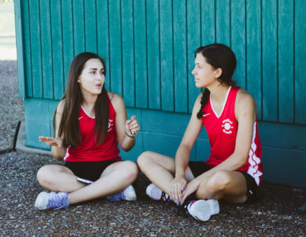 Photo of two teenage girls in soccer uniforms sitting and talking