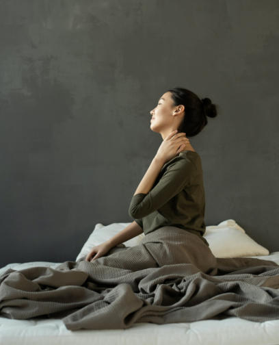 Photo of woman sitting on her bed holding her neck in pain