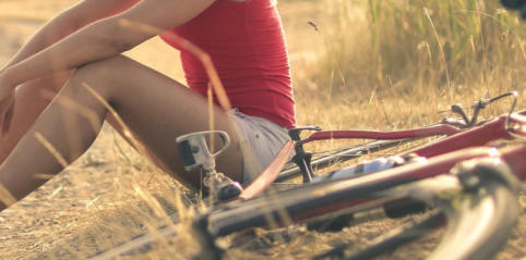 Image of woman sitting on the ground next to a bike lying on its side