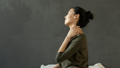Photo of woman sitting on her bed holding her neck in pain